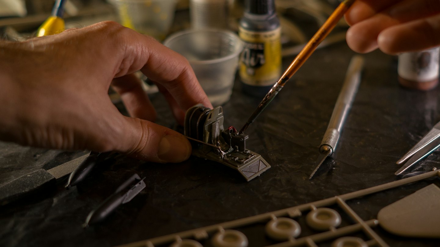 Manos pintando un detallado interior de cabina de avión en miniatura con pincel fino.